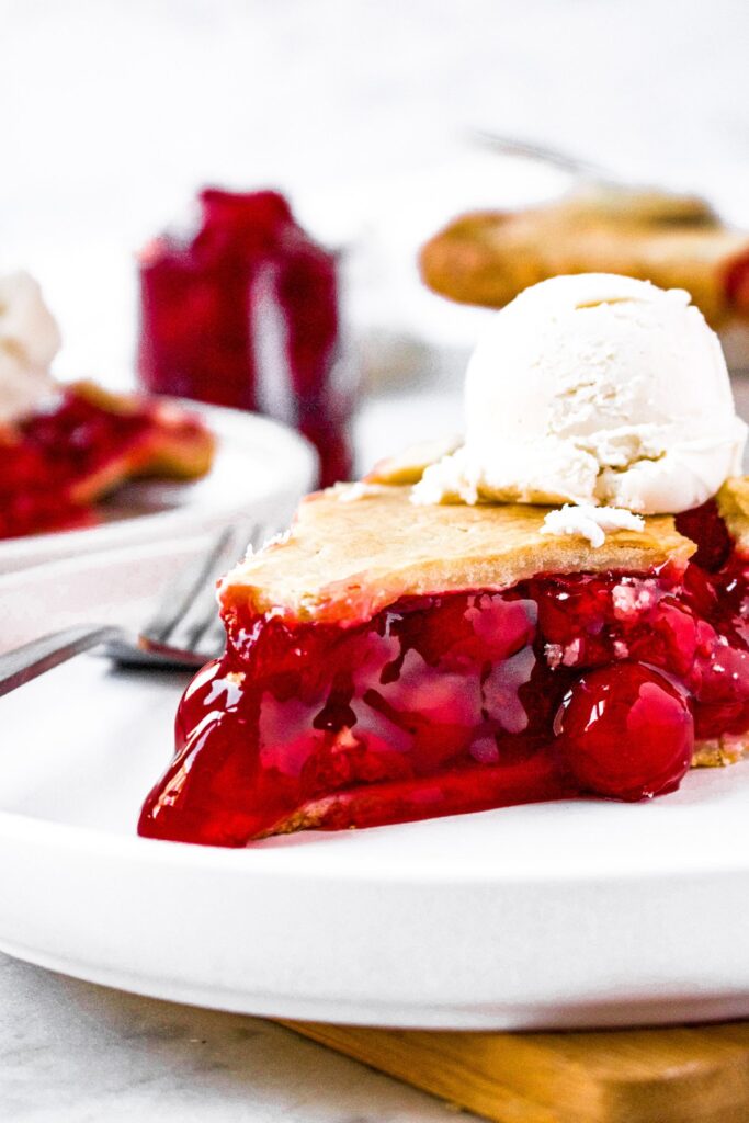 Close up head-on photo of a slice of cherry pie with vegan ice cream on top