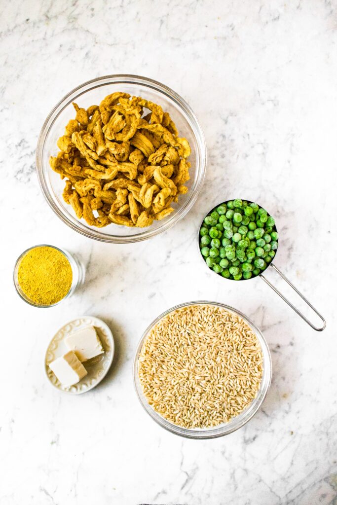 Overhead shot of the 5 ingredients in crockpot vegetarian chicken and rice recipe: long grain brown rice, dairy free butter, vegan chicken bouillon powder, frozen peas, and soy curls.