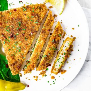 Close up overhead shot of a sliced crispy breaded tofu cutlet sprinkled with herbs and crushed red pepper