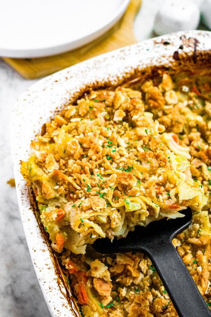 Overhead shot of a spatula lifting a slice of vegan chicken noodle casserole out of a casserole dish.