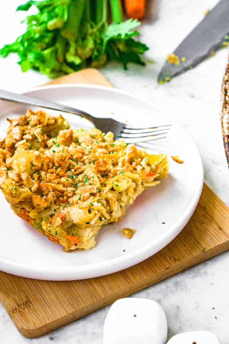 Overhead shot of a slice of vegan chicken noodle casserole on a plate with a fork sitting next to it and celery peeking in the back.