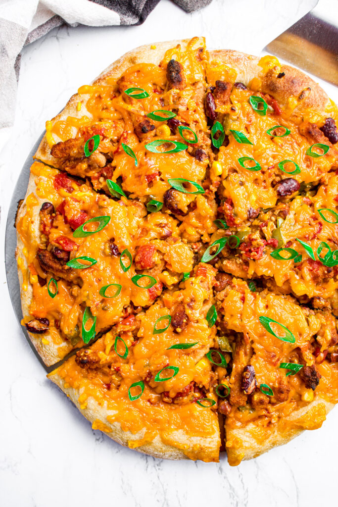 Overhead view of half a sliced vegan chili cheese fry pizza topped with sliced green onions