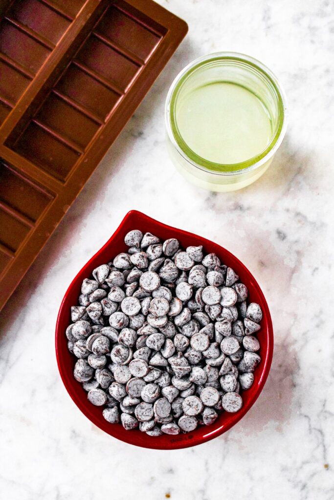Overhead shot of the ingredients you need to make vegan chocolate bars: dairy-free chocolate chips, refined coconut oil, and silicone chocolate bar mold