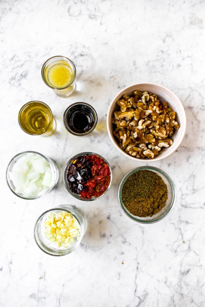 Overhead shot of all the ingredients you need to make vegan chorizo walnut meat: raw walnuts, dried chilis, sun-dried tomatoes, onion, garlic, olive oil, lime juice, soy sauce, and spices