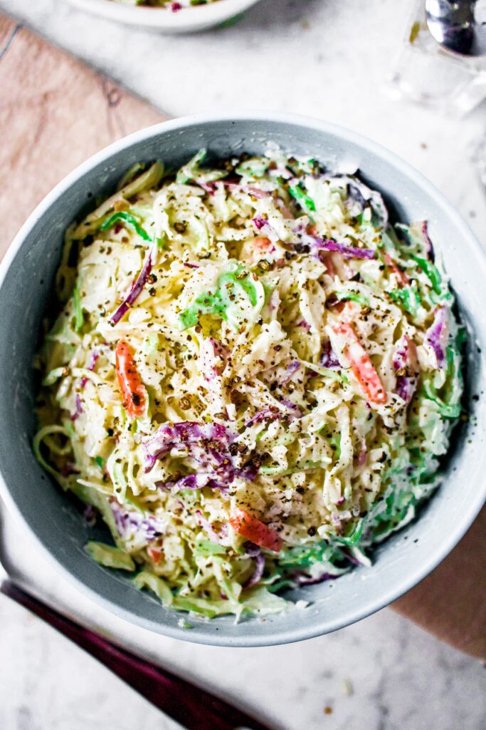 Overhead shot of a bowl of creamy dairy free coleslaw. There is a folded beige linen under the bowl