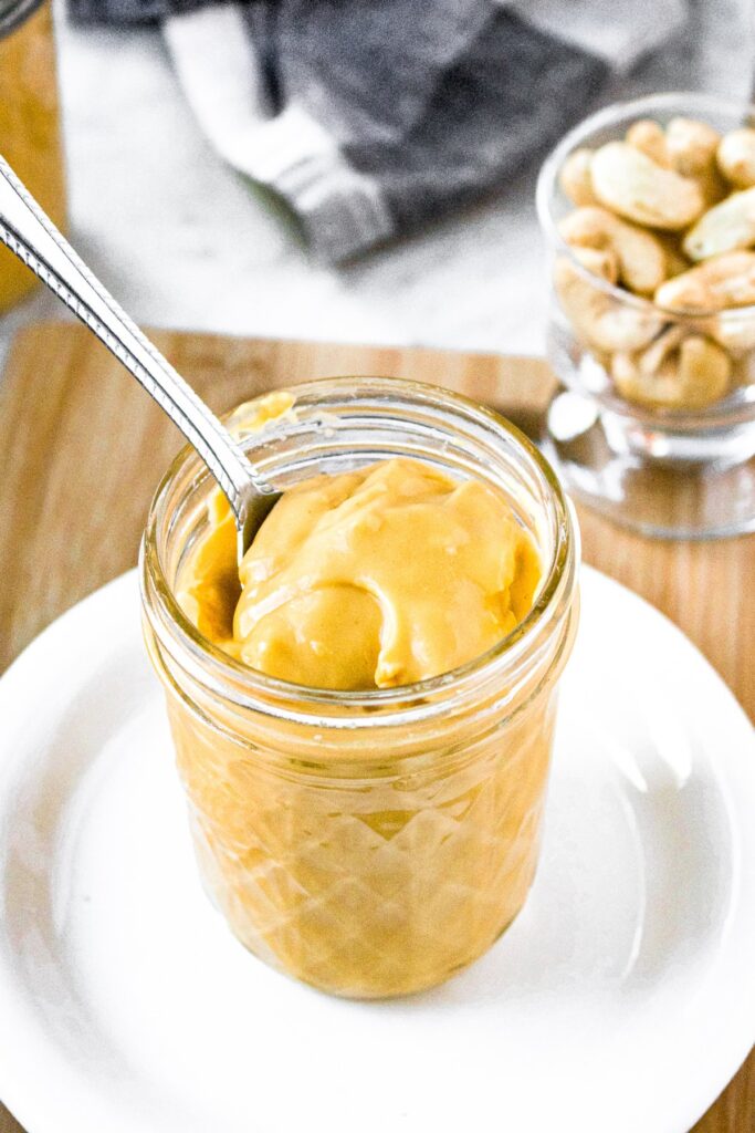 Overhead photo of a small glass jar of plant-based cheddar cheese soup with a spoon going into it to show the thick and creamy dairy-free texture.