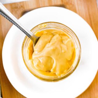 Overhead shot of a clear glass jar filled with vegan condensed cheese soup. There is a spoon digging into the soup to show the creamy thick texture.