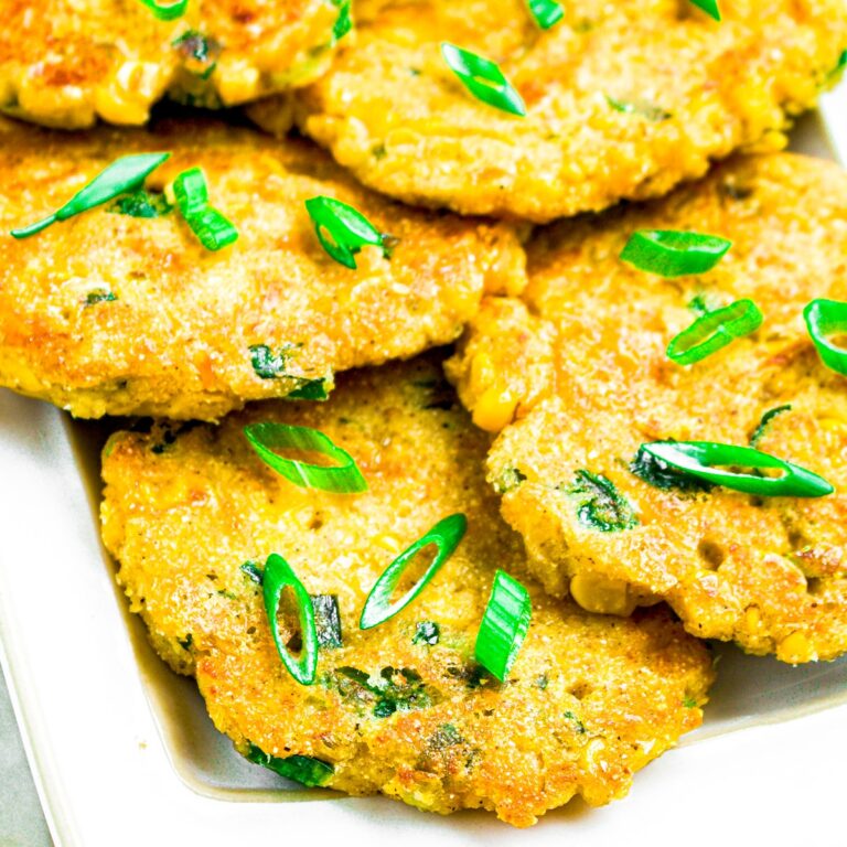 A pile of vegan corn fritters sprinkled with sliced green onions arranged on a long white plate