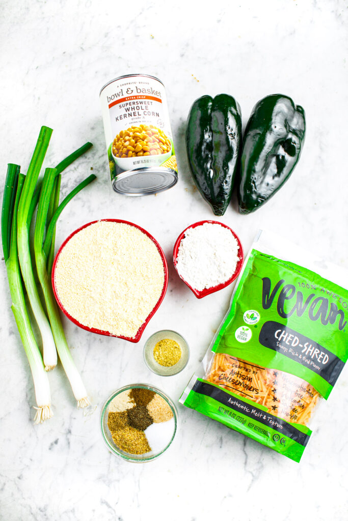 Ingredients photo with can of corn, cornmeal, flour, green onions, bag of vegan cheddar, spices, and poblano peppers