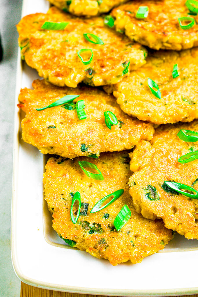 A head on photo of a long white rectangular plate of vegan poblano corn cakes topped with sliced scallions