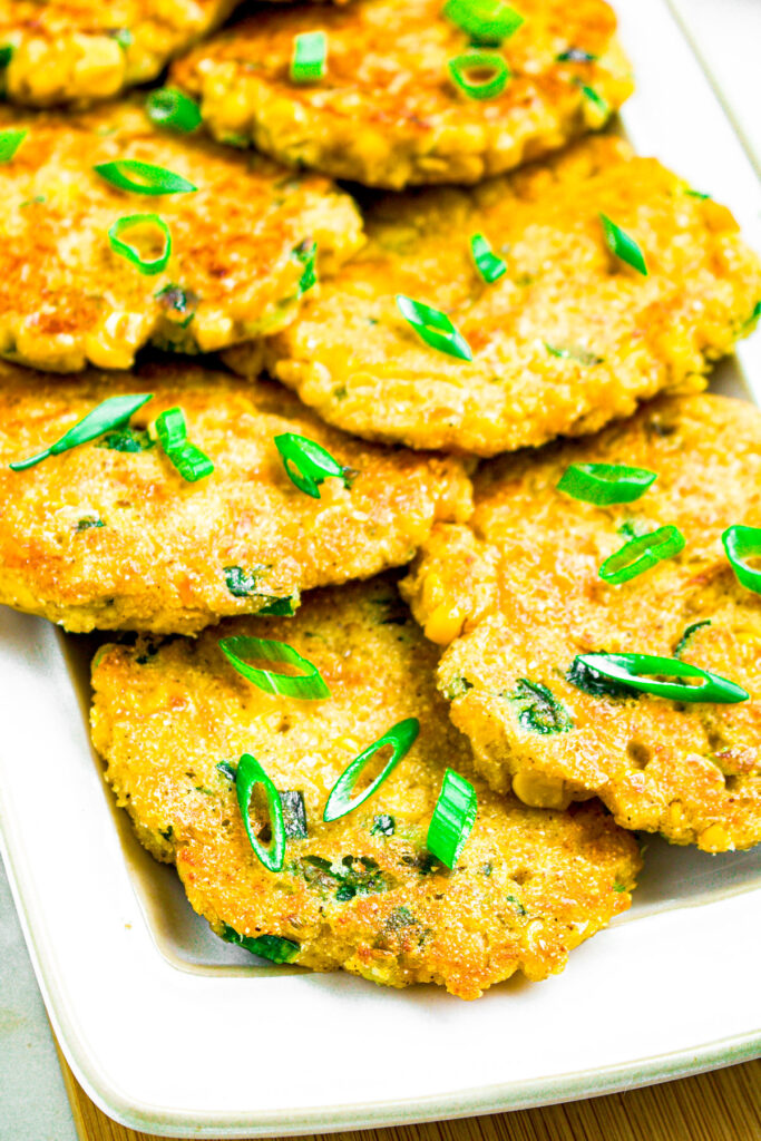 Overhead close up photo of part of a long white plate piled high with easy vegan corn fritters with sliced spring onion on top