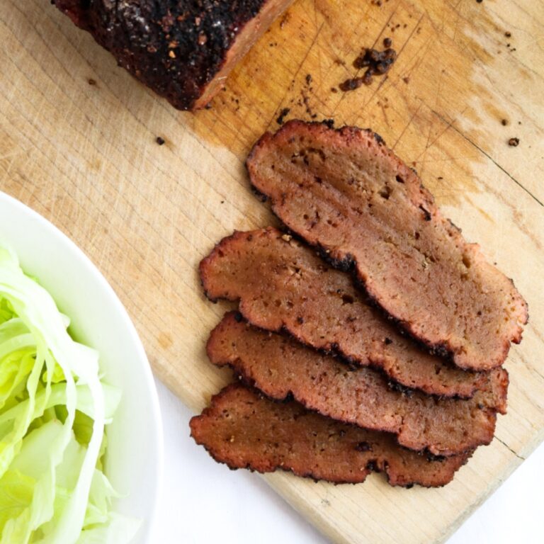 Overhead view of four thin slices of corned beef seitan fanned out on a wood cutting board