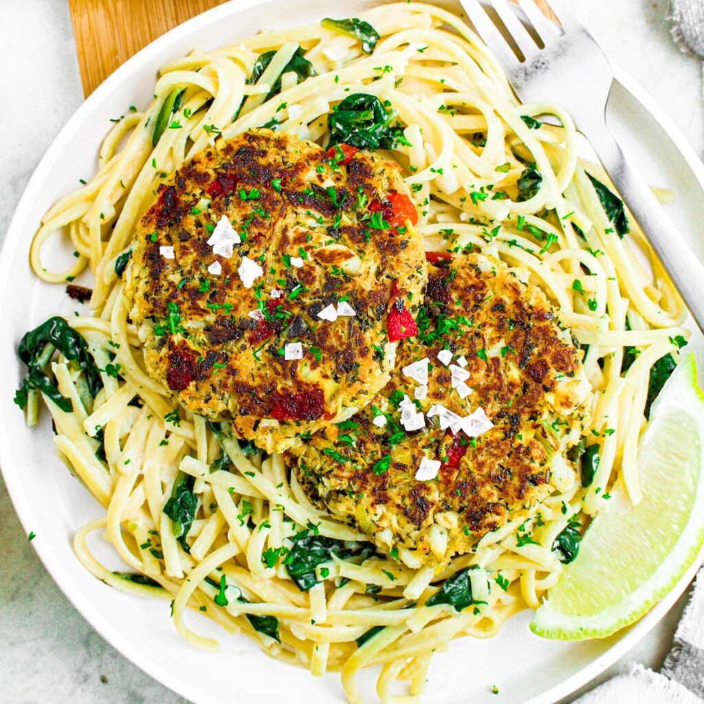 Close up overhead photo of a plate of vegan crab cakes on top of creamy spinach spaghetti