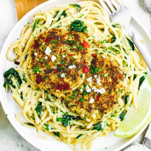 Close up overhead photo of a plate of vegan crab cakes on top of creamy spinach spaghetti