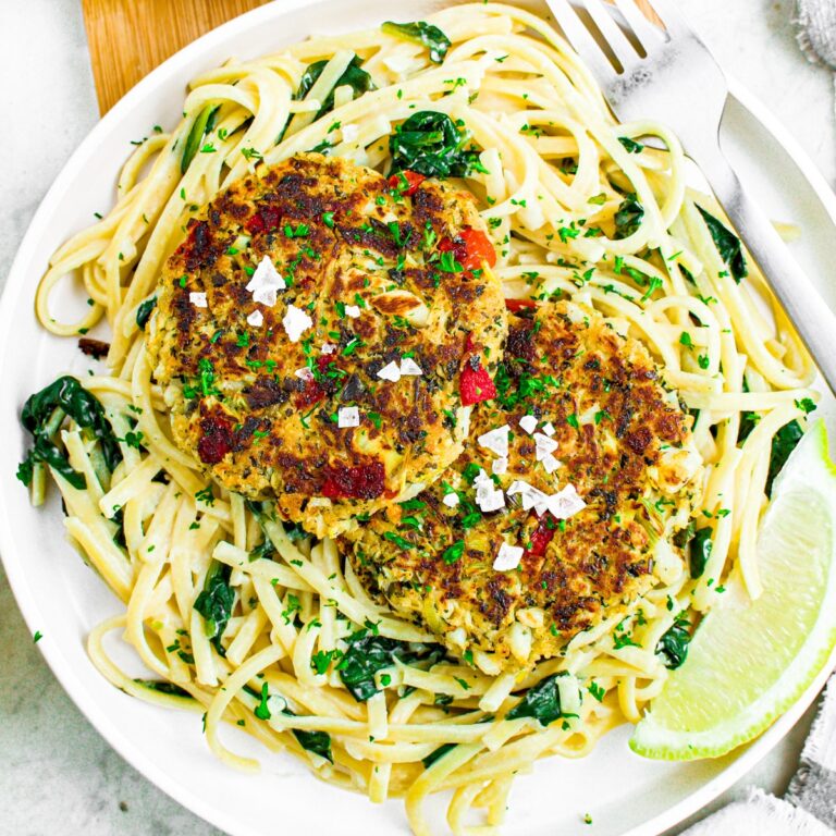 Close up overhead photo of a plate of vegan crab cakes on top of creamy spinach spaghetti