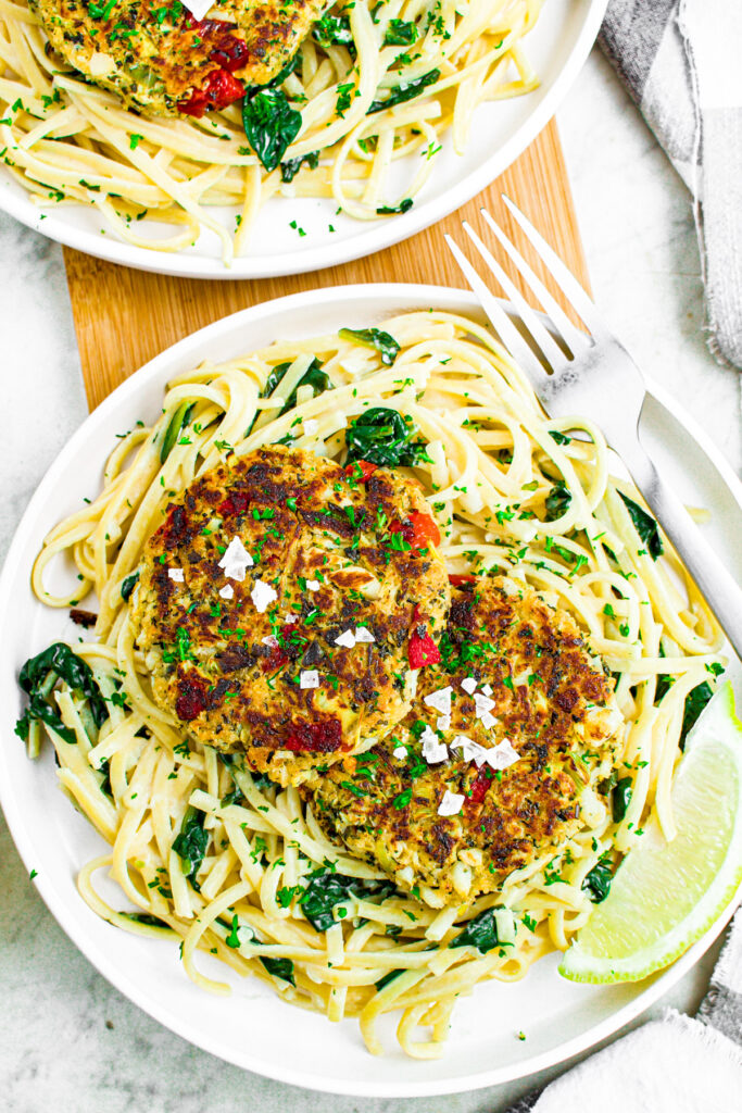 Overhead photo of a round white plate of creamy spinach pasta with two vegan crab cakes on top