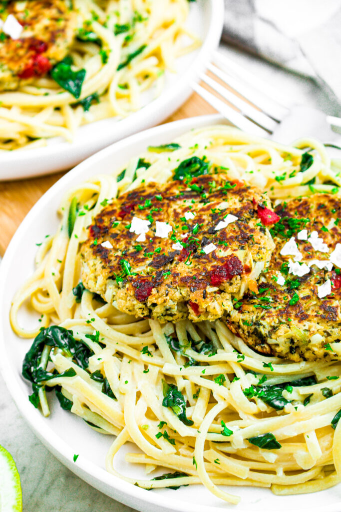 Overhead photo of a vegan crab cake sprinkled with sea salt atop a plate of spinach pasta