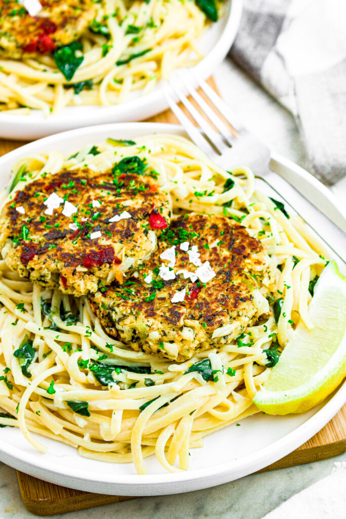 Overhead photo of 2 hearts of palm crab cakes on a plate with creamy pasta and a lemon wedge
