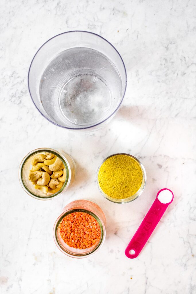 An overhead photo of the ingredients needed to make vegetarian and dairy free condensed cream of chicken soup substitute: water, cashews, red lentils, vegan chicken bouillon powder, and salt.