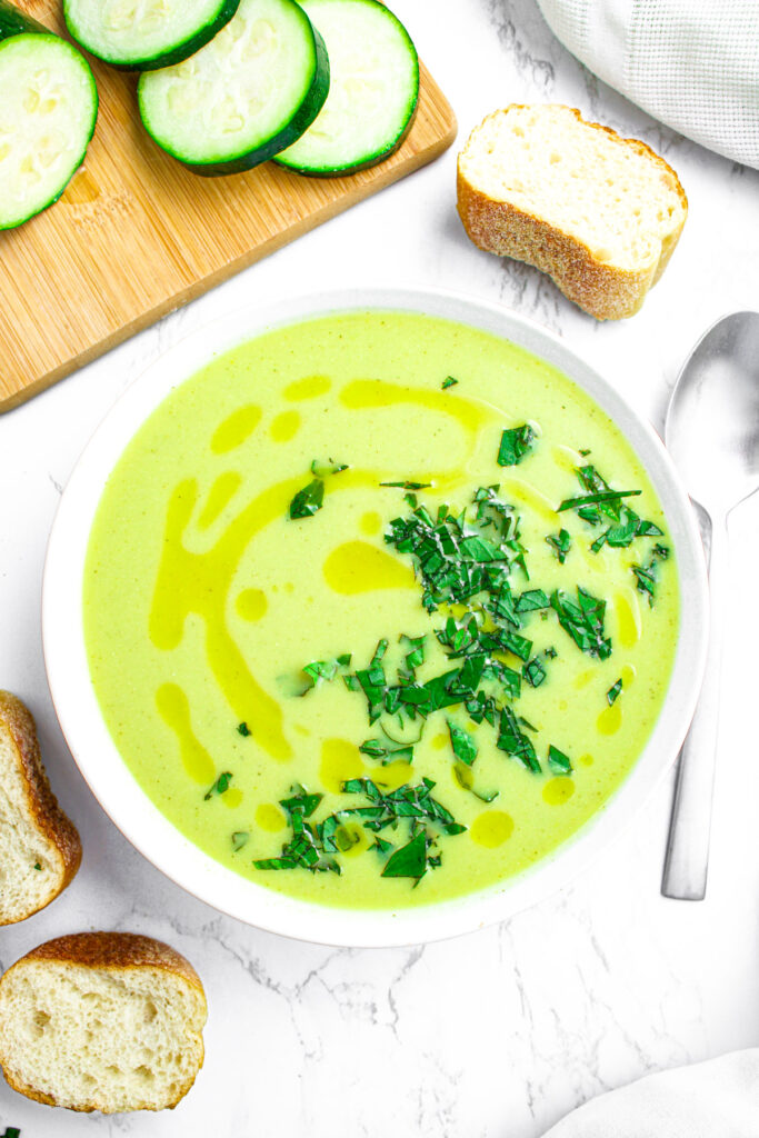 Overhead view of a round white bowl filled with creamy zucchini soup topped with fresh basil