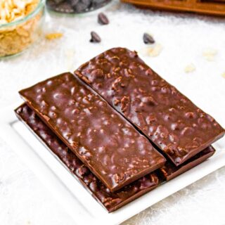 Overhead photo of a tower of homemade crunch bars on a plate. There is a bowl of chocolate chips and rice cereal behind the bars.