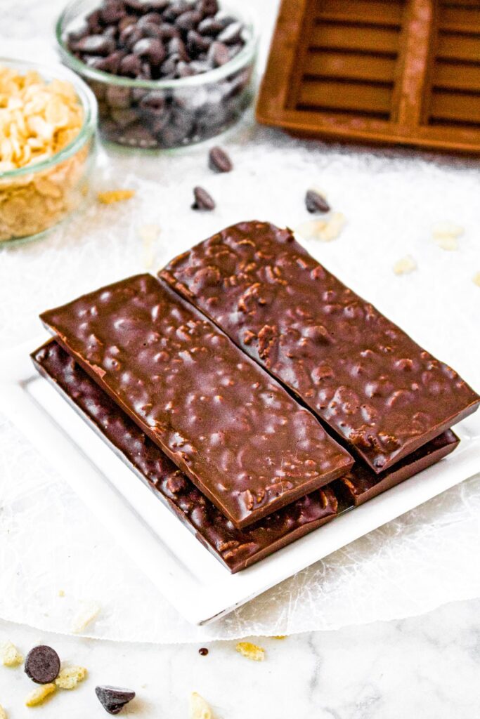 Overhead photo of a tower of homemade crunch bars on a plate. There is a bowl of chocolate chips and rice cereal behind the bars.