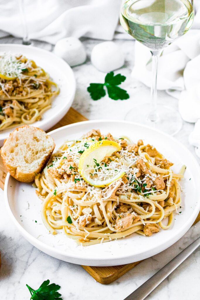 Head on shot of a plate of vegan linguine clam sauce topped with fresh green herbs and a twisted lemon rind