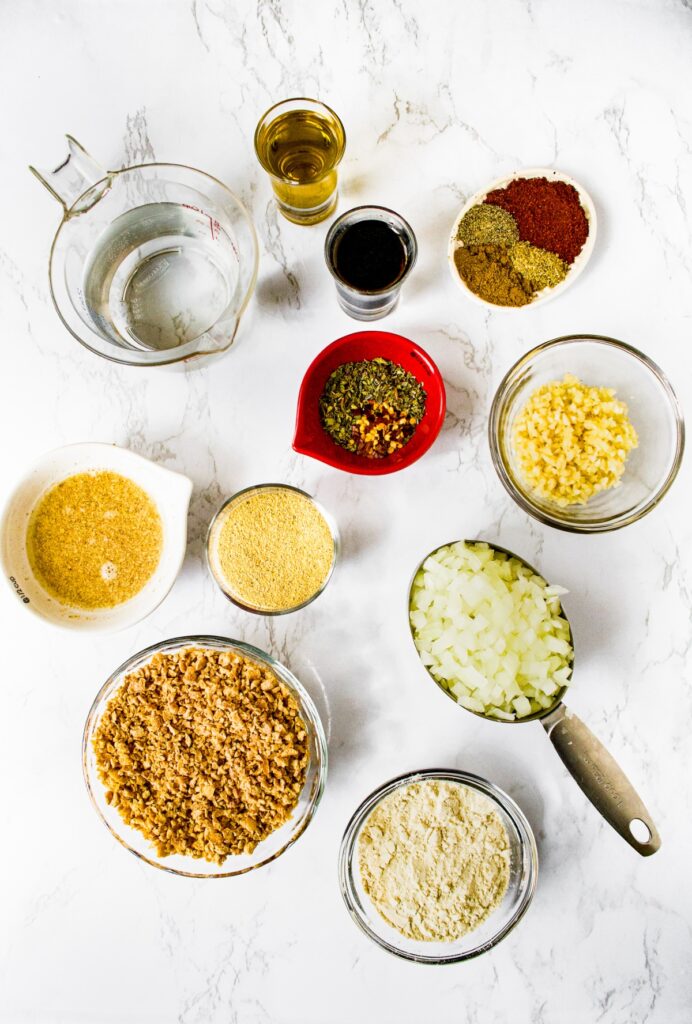 An overhead shot of all the ingredients you need to make the best homemade vegan meatballs: TVP, onion, vital wheat gluten, flaxseed egg, nutritional yeast, garlic, water, olive oil, soy sauce, Italian seasoning, chili powder, crushed red pepper flakes, pepper, onion powder, and ground cumin
