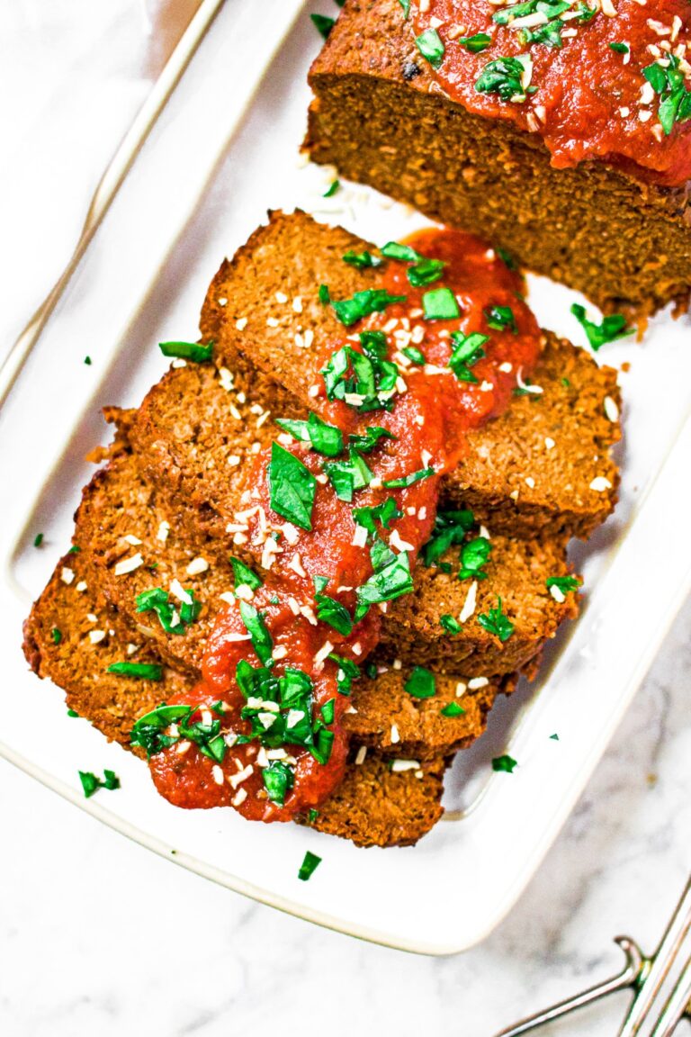 Overhead photo of a partially sliced vegan meat loaf on a white rectangular plate