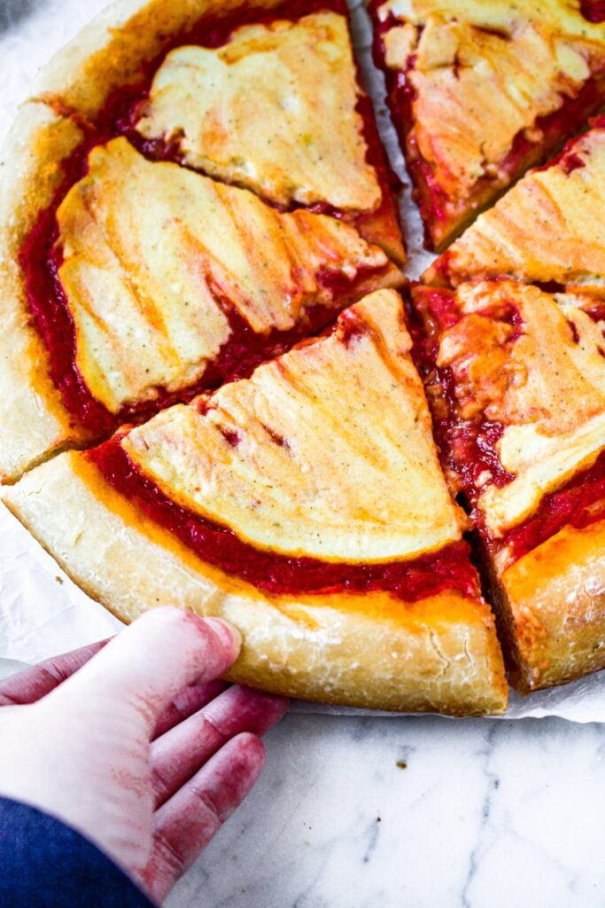 Overhead shot of a vegan cheese pizza, sliced, with a hand pulling one slice out.