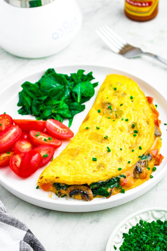 Close up photo of a plate with a plant based omelet on it, folded over with mushroom and spinach filling pouring out