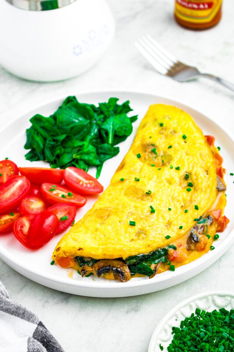 Close up photo of a plate with a plant based omelet on it, folded over with mushroom and spinach filling pouring out