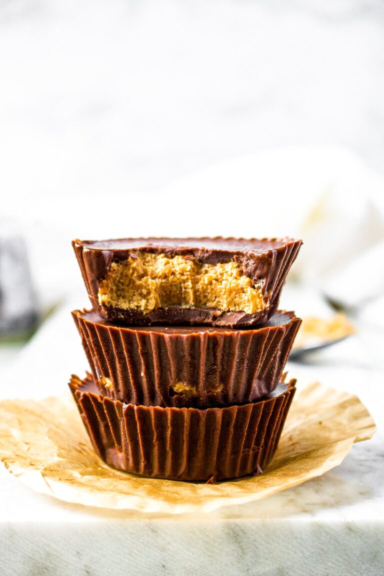 Head on shot of 3 peanut butter cups stacked on top of each other with a bite taken out of the top one, showing the peanut butter filling.