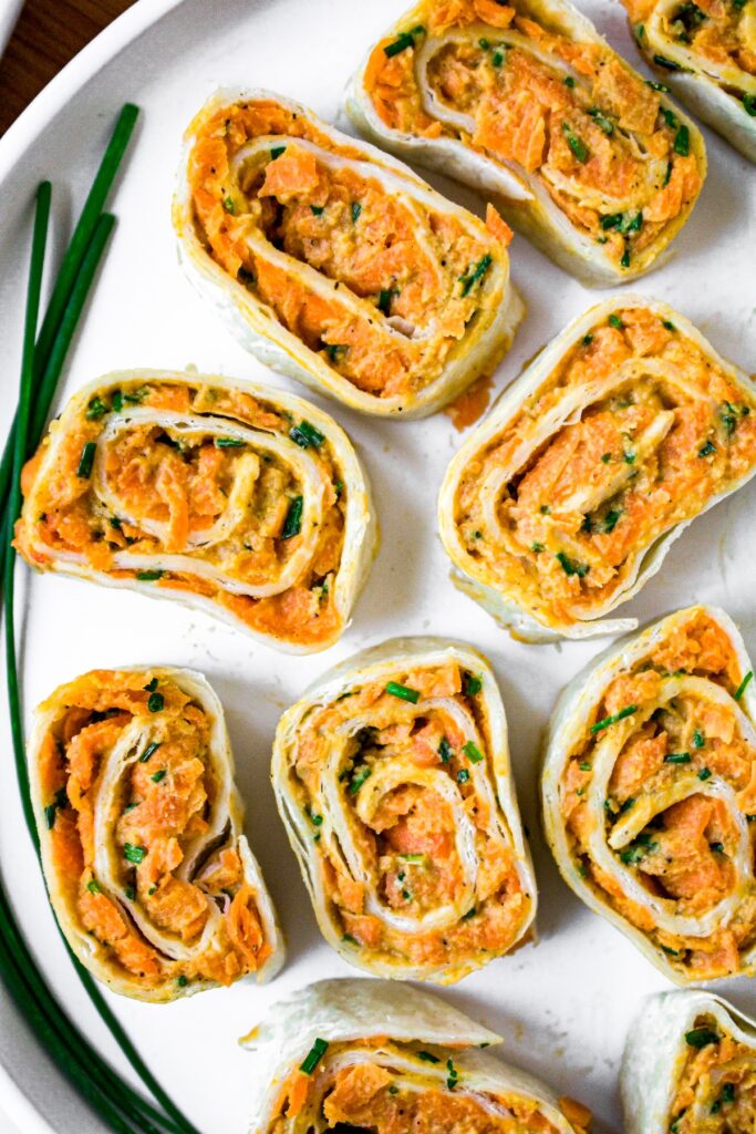 Close up overhead shot of 9 tortilla pinwheels on half a round plate with a fresh green onion off to the side.