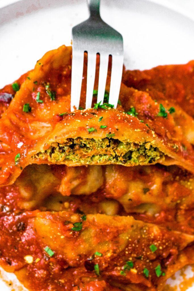 Close up shot of a vegan ravioli square cut in half showing the dairy free spinach and tofu ricotta filling.
