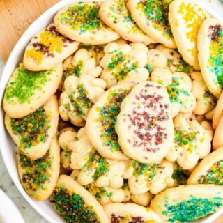 Close up overhead photo of a round plate of vegan butter cookies decorated with purple, blue, green, and yellow sugar