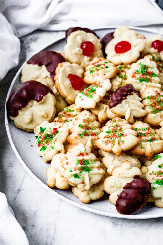 Overhead photo of a round plate piled high with vegan spritz cookies decotated for the holiday season