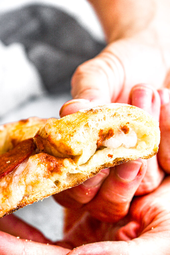 Head on view of a white hand holding a slice of pizza with a stuffed crust