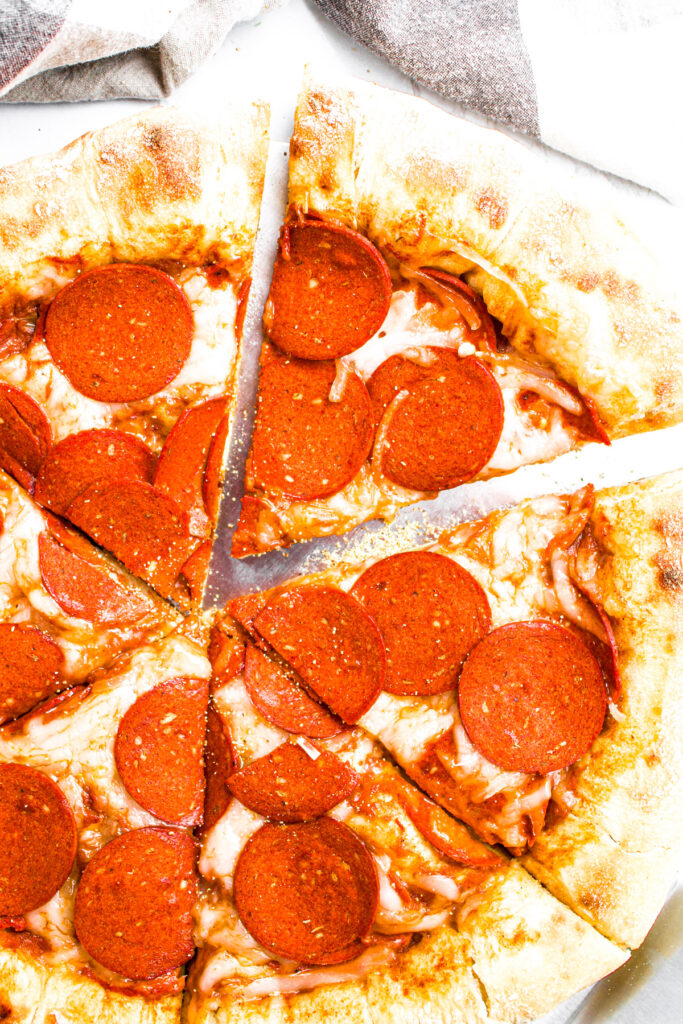 Overhead view of a sliced vegan pepperoni pizza with one slice pulled out