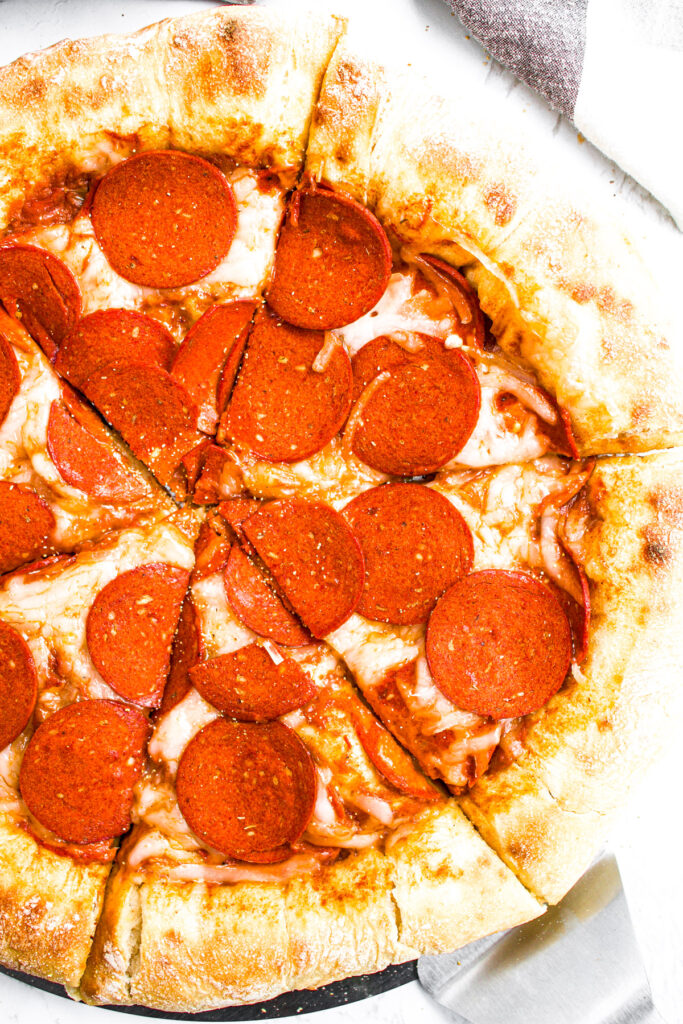 Overhead view of half a sliced vegan pepperoni pizza with a big fluffy stuffed pizza crust