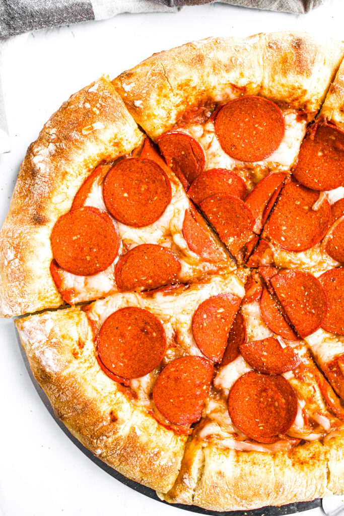 Overhead view of half a sliced plant-based pepperoni pizza with a big golden brown stuffed mozzarella crust