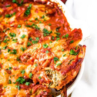 Head on close up photo of a large spoon scooping a vegan stuffed shell out of a baking dish
