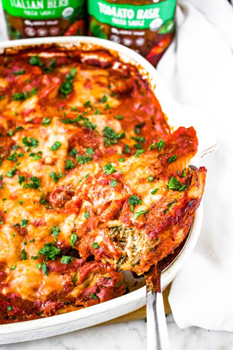 Head on close up photo of a large spoon scooping a vegan stuffed shell out of a baking dish