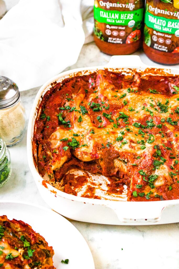 Head-on shot of a baking dish filled with freshly baked tofu ricotta stuffed shells with the front left corner scooped out onto a plate next to the dish