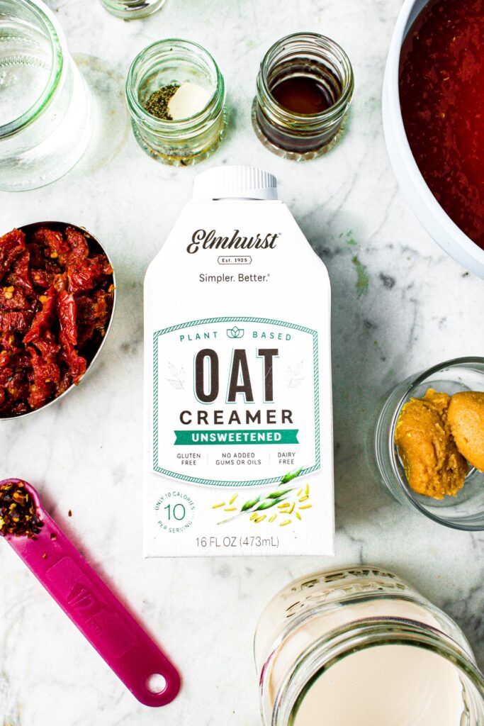 Overhead shot of a small carton of Elmhurst unsweetened oat creamer surrounded by the ingredients you need to make vegan vodka pasta