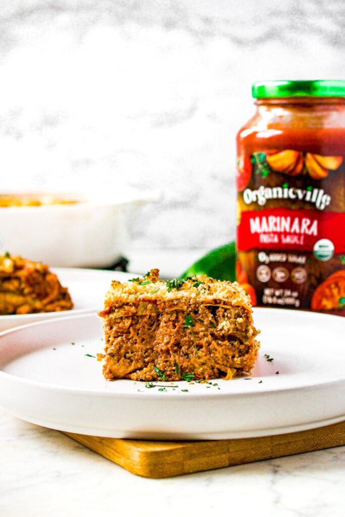 Head on shot of a slice of meatless zucchini lasagna on a plate sprinkled with fresh minced herbs. There is a jar of marinara sauce in the background.