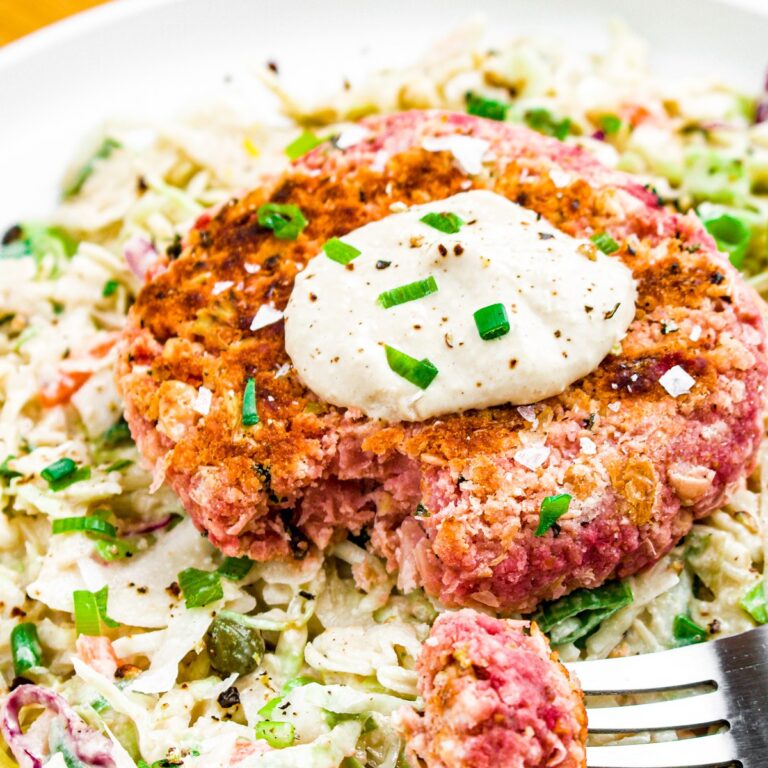 Close up head on photo of a partially bitten into vegan salmon burger topped with chopped green onions and aioli