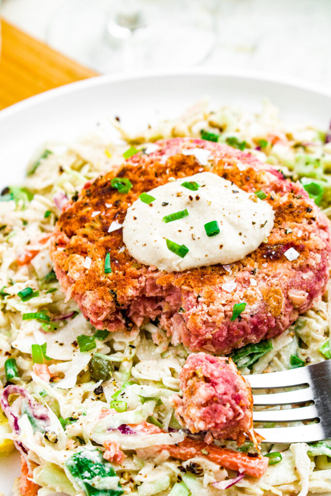 Close up head on photo of a vegan salmon burger on a bed of tahini slaw topped with a creamy aioli