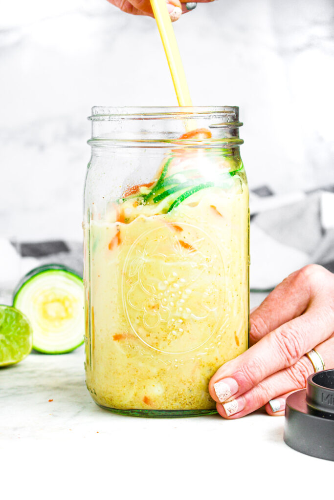 Head on photo of a large glass mason jar with creamy curry veggie ramen in it