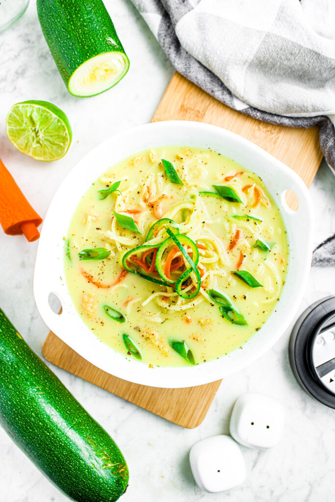 Overhead photo of a bowl of creamy zoodle ramen surrounded by zucchini, lime, and carrot pieces